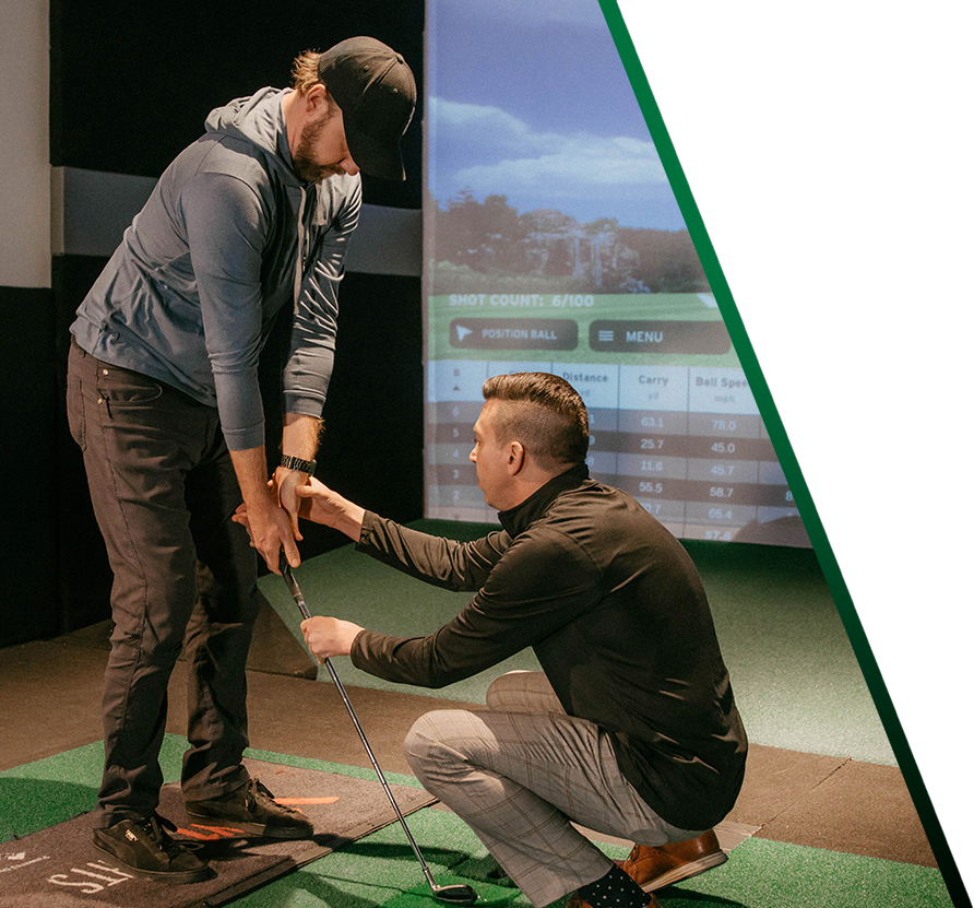 An instructor kneels in front of a golfer, showing him how to hold his club.