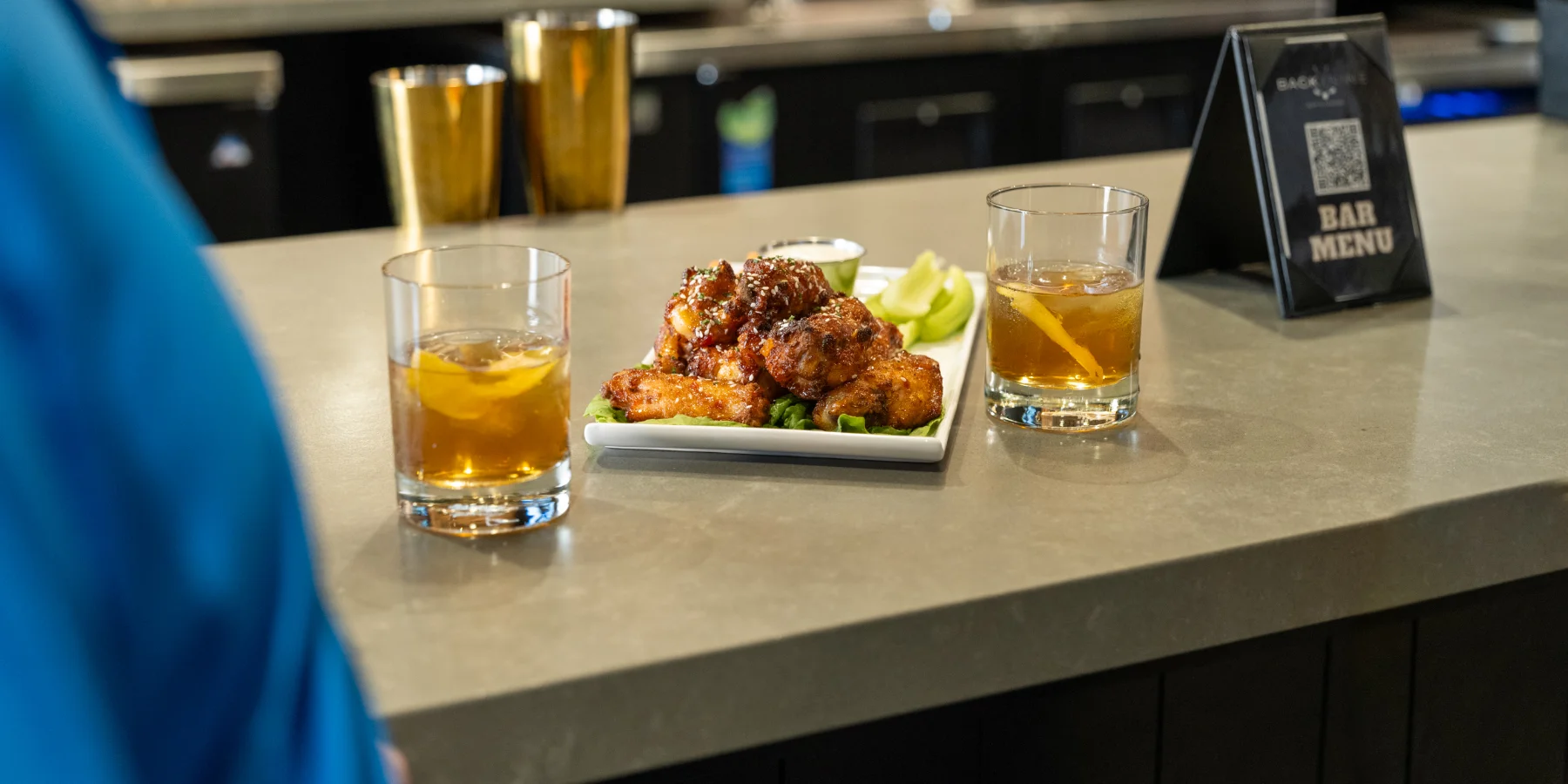 A plate of wings and a couple cocktails sit on the bar at X-Golf.